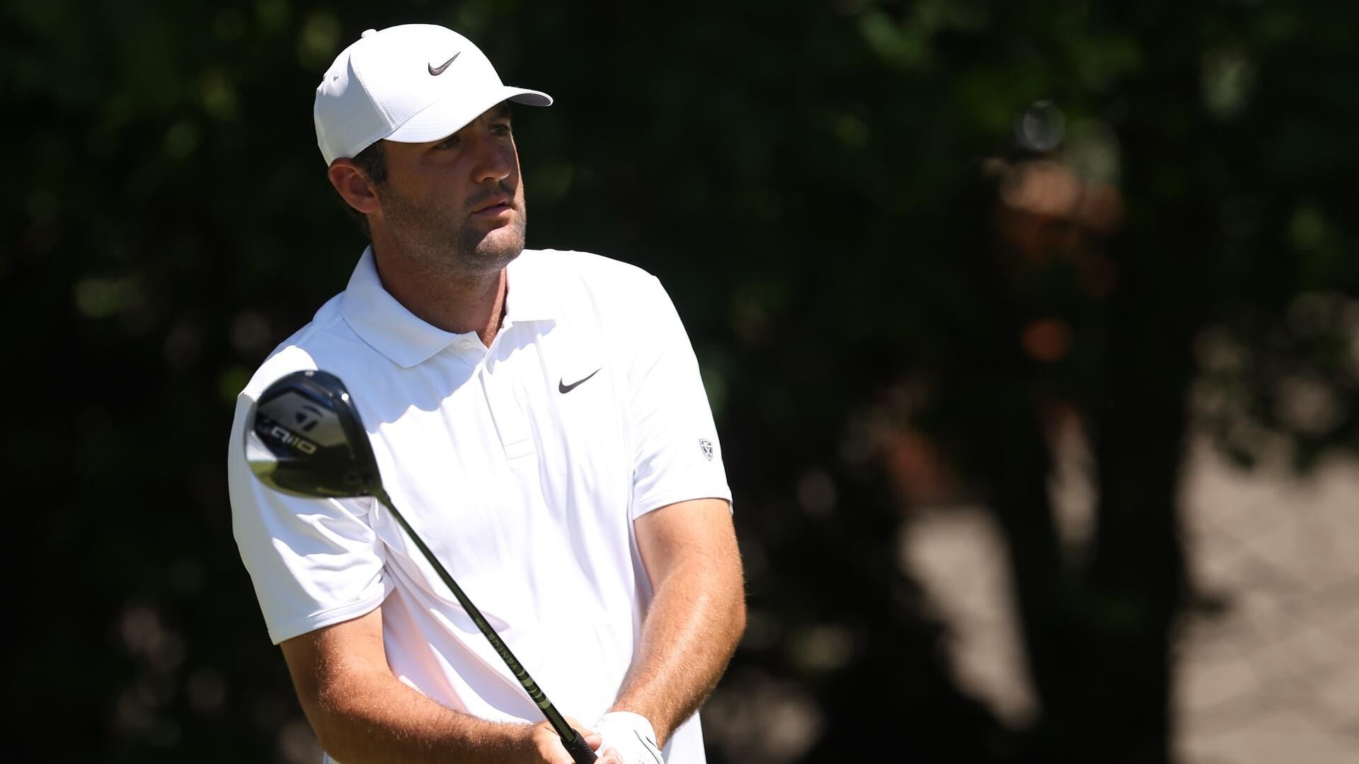 A golfer in a white Nike cap and polo shirt watches his tee shot, holding a driver on a sunlit course.