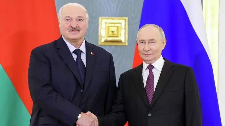 Two men in dark suits shake hands in front of a red-and-green flag and a white-blue-red flag.