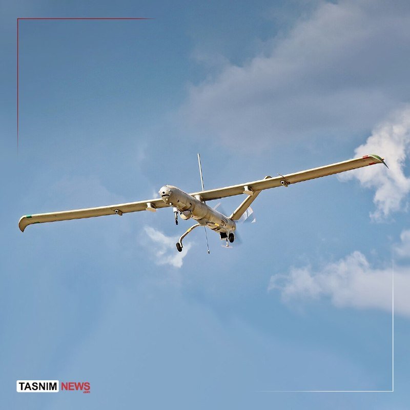 A white unmanned aerial vehicle with long wings flies through a partly cloudy blue sky.