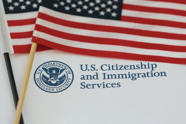 Two small American flags rest atop a document displaying the U.S. Department of Homeland Security seal and "U.S. Citizenship and Immigration Services" text.