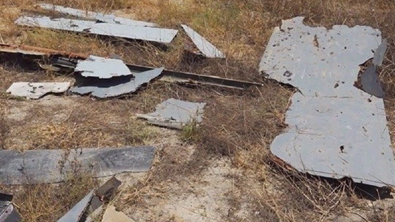 Scattered metal debris lies across dry grass and sandy ground.