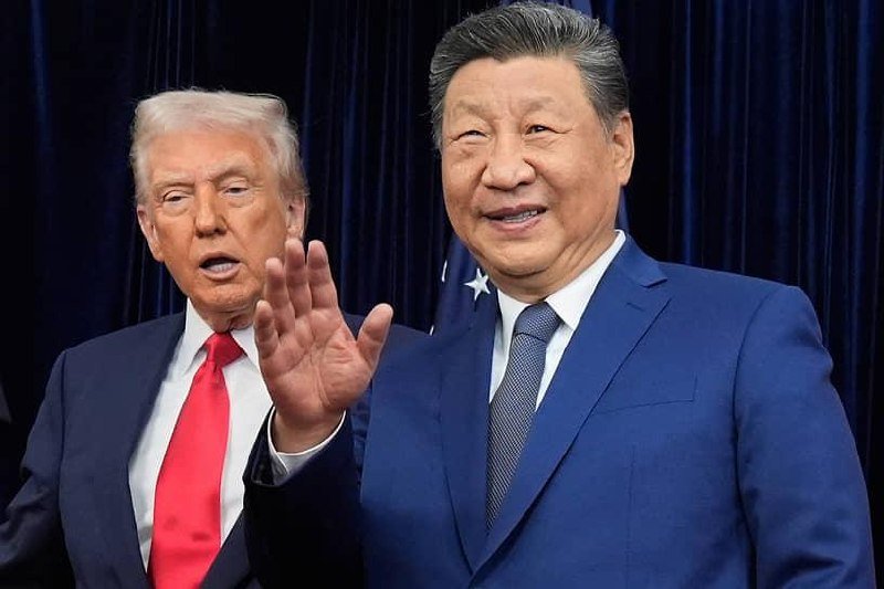 Two men in suits stand side by side before dark blue curtains, with the American flag partially visible behind them; one gestures with an open hand while the other smiles.