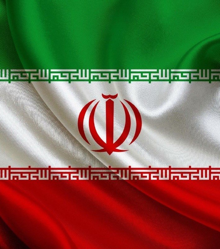A close-up image of the Iranian flag, showing green, white, and red horizontal stripes with the red national emblem in the center, displayed as a rippled fabric graphic.