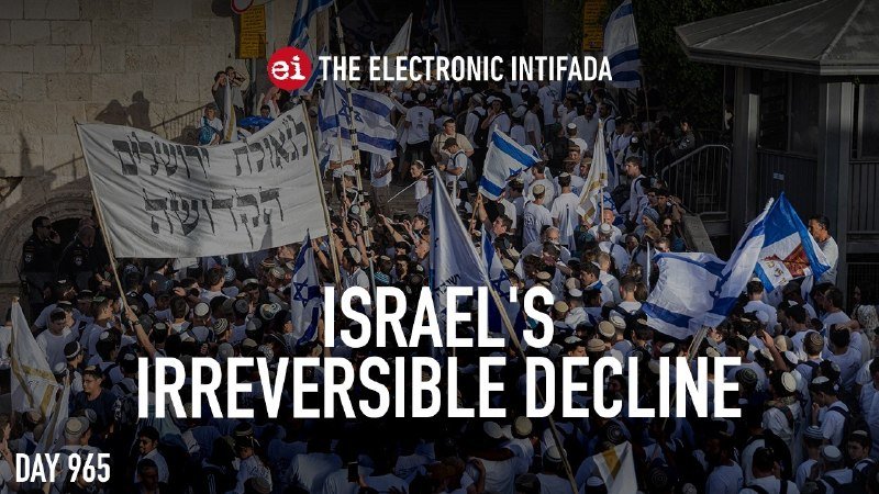 A large crowd waves Israeli flags and banners in a stone-paved plaza, overlaid with the text "THE ELECTRONIC INTIFADA" and "ISRAEL'S IRREVERSIBLE DECLINE."