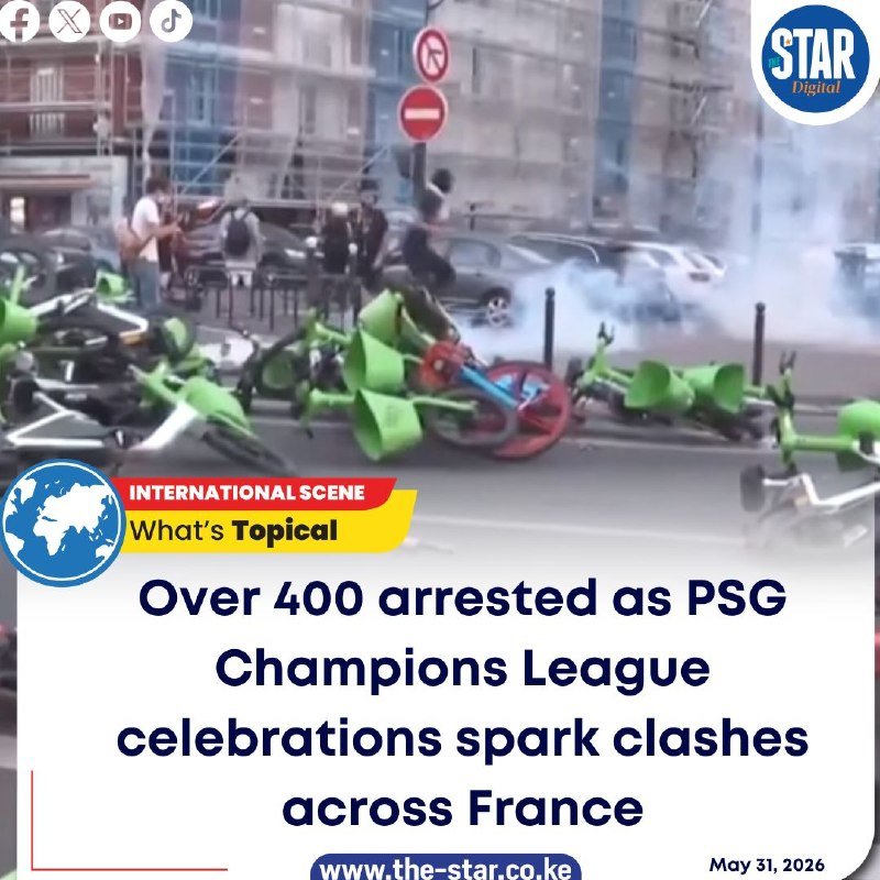 Toppled green rental bicycles lie scattered across a street as smoke rises in the background, with a headline reading "Over 400 arrested as PSG Champions League celebrations spark clashes across France."