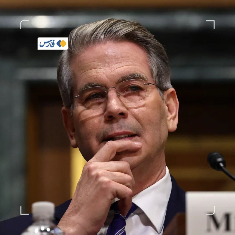 A gray-haired man in glasses, suit, and tie rests his chin on his hand near a microphone.