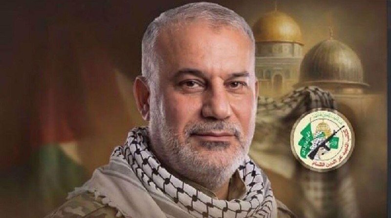 A digital illustration shows a gray-bearded man wearing a black-and-white checkered scarf, posed before a domed structure and a circular green-and-white emblem.