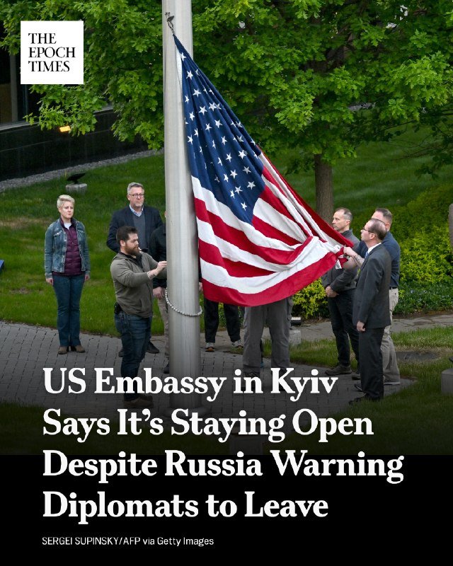 Several people raise an American flag up a flagpole outdoors, with the text "The Epoch Times" logo in the corner.