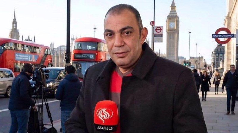 A man speaks into an Al Mayadeen microphone in London, with Big Ben, red double-decker buses, and an "Underground" sign visible behind him.