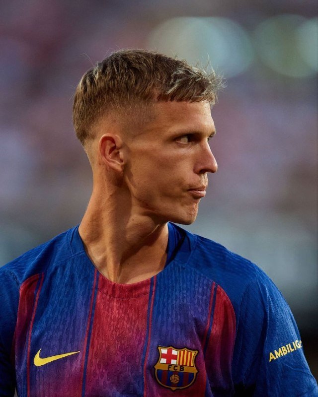 A blonde-haired soccer player in a blue and red striped FC Barcelona jersey looks off to the side during a match.