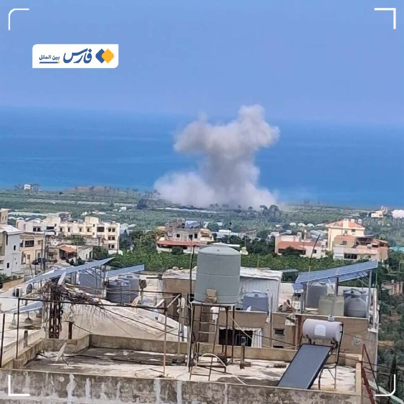 A plume of white smoke rises above a coastal town with rooftop water tanks and solar panels, with Arabic text in the upper corner.