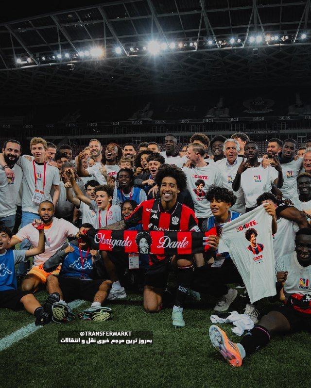 A large group of soccer players and staff in white and red-and-black jerseys celebrate on a stadium pitch, with one player holding a scarf reading "Obrigado Dante."