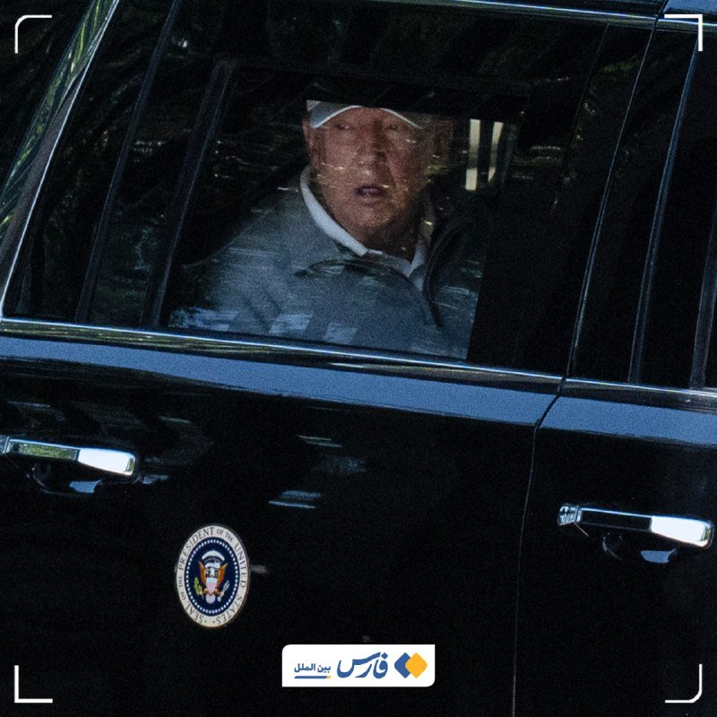 A man wearing a white cap sits in the back of a black vehicle bearing the Presidential Seal of the United States.