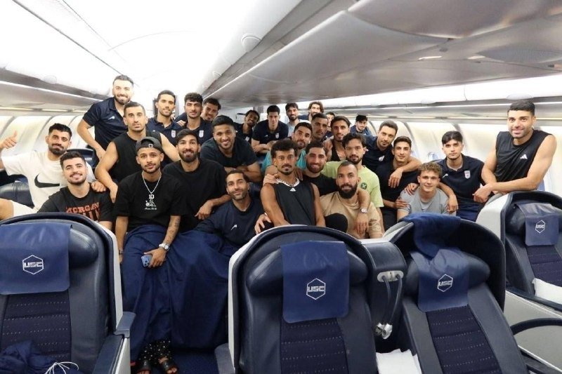 A large group of men poses for a group photo inside an airplane cabin, with "USG" visible on seat headrests.