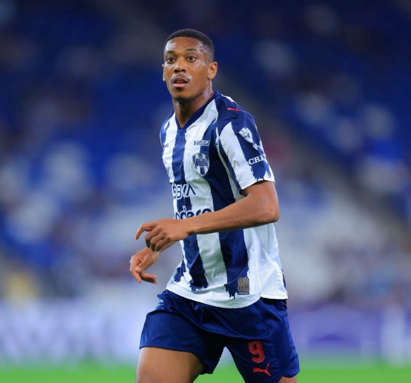 A soccer player wearing a blue and white striped jersey with the number 9 looks upward during a match in a stadium.