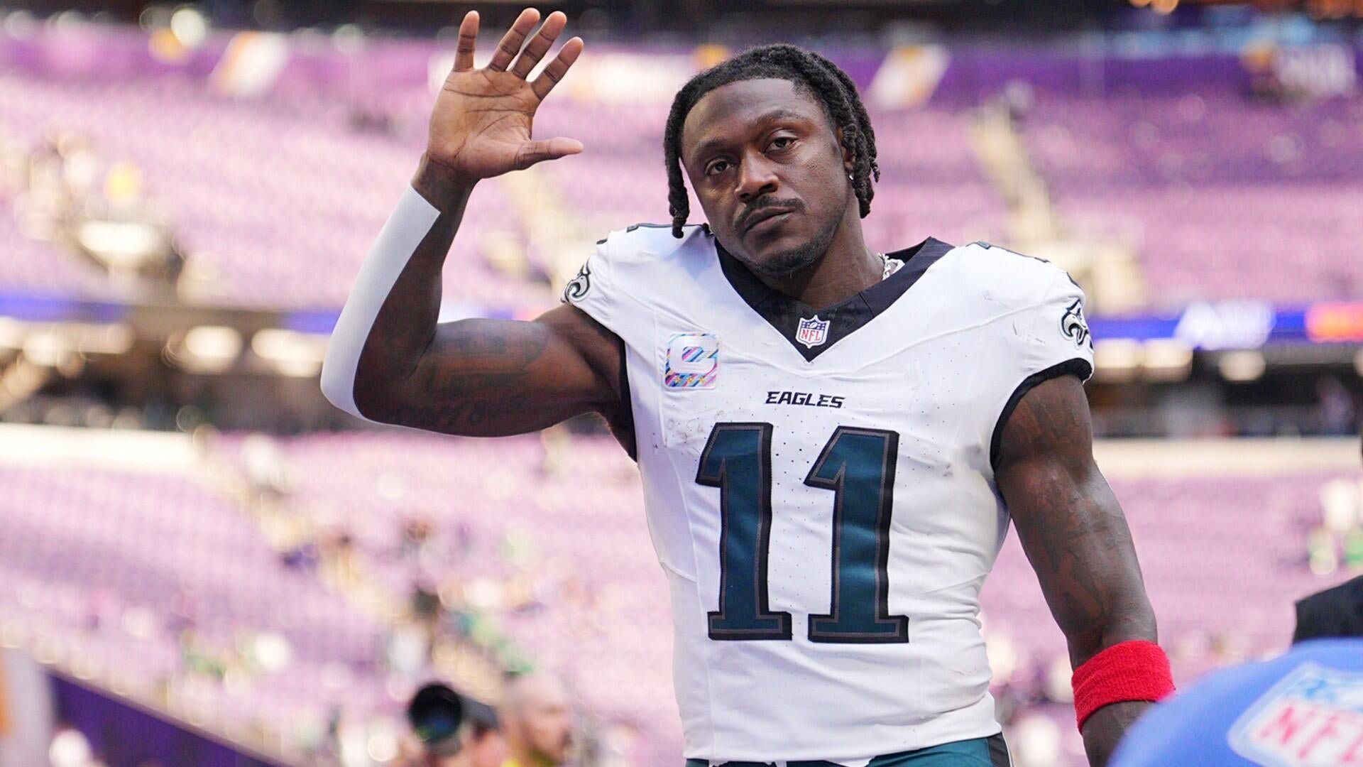 A football player wearing a white Eagles jersey with the number 11 waves to fans inside a stadium.