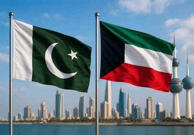 The flags of Pakistan and Kuwait fly side by side on flagpoles, with a modern city skyline and distinctive towers visible across the water in the background.