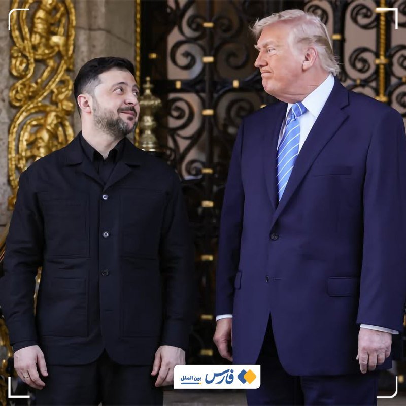 Two men stand side by side before ornate golden gates, one in a black jacket looking up at the other, who wears a navy suit and blue striped tie.