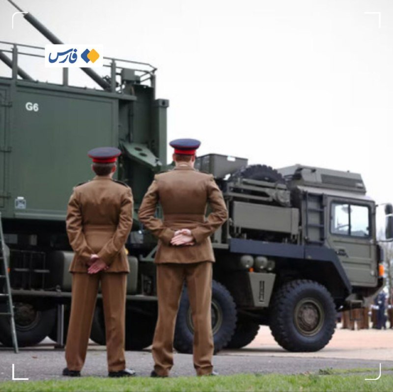 Two military personnel in brown uniforms and peaked caps stand at attention with hands behind their backs before a large green "G6" labeled military vehicle.