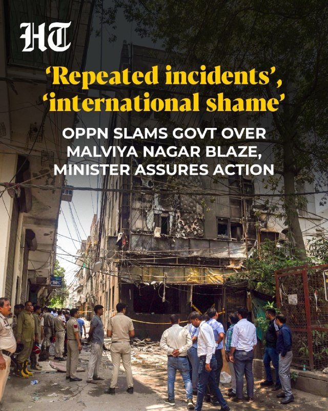 A burnt-out building stands in a narrow street as police officers and onlookers gather at the scene.