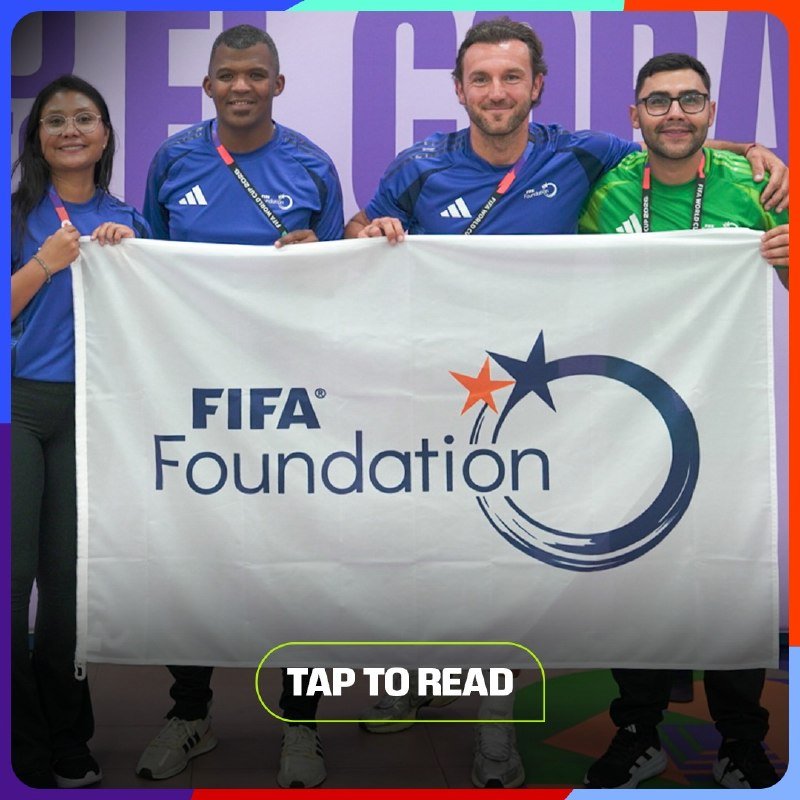 Four people in blue and green shirts hold a FIFA Foundation flag.