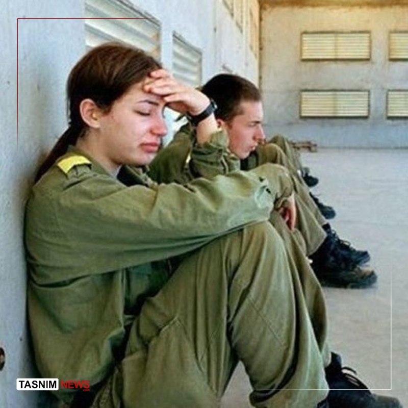 Three soldiers in combat gear stand atop a tank holding weapons and a yellow Hezbollah flag, with the Tasnim News logo visible in the corner.