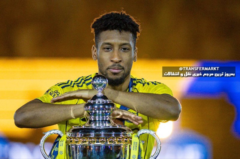 A young man with a beard, wearing a yellow jersey, holds a large silver trophy while crossing his arms over it against a blurred background.
