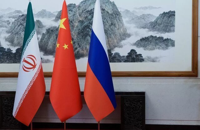 Three national flags—Iran, China, and Russia—stand side by side on poles in front of a framed Chinese landscape painting.