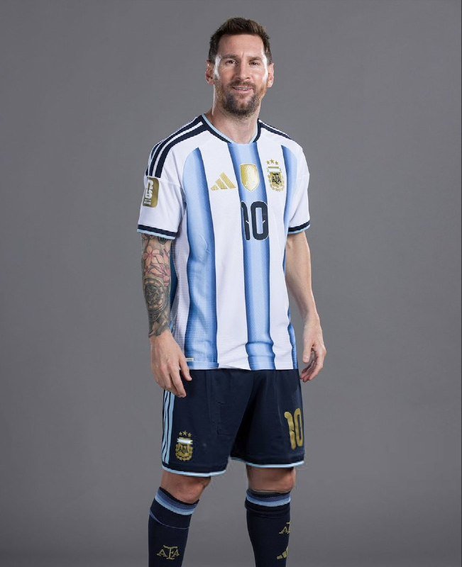 A bearded man poses against a gray background wearing a light blue and white striped Argentina national team jersey and black shorts, both displaying the number 10 and federation crest.