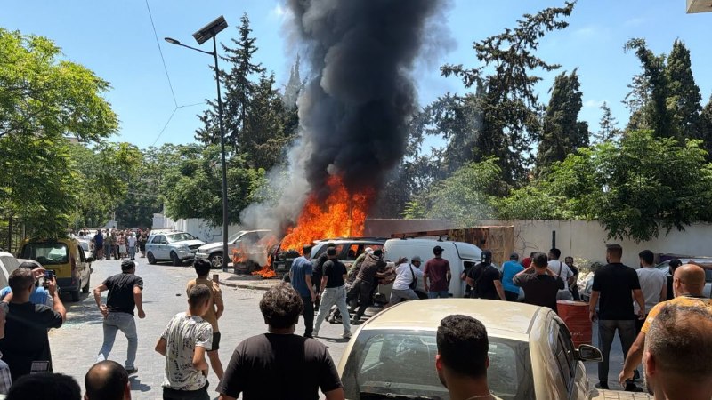 A car with smiling passengers waving Iranian and Hezbollah flags travels past a building, above a French text quote attributed to Hezbollah's guide.