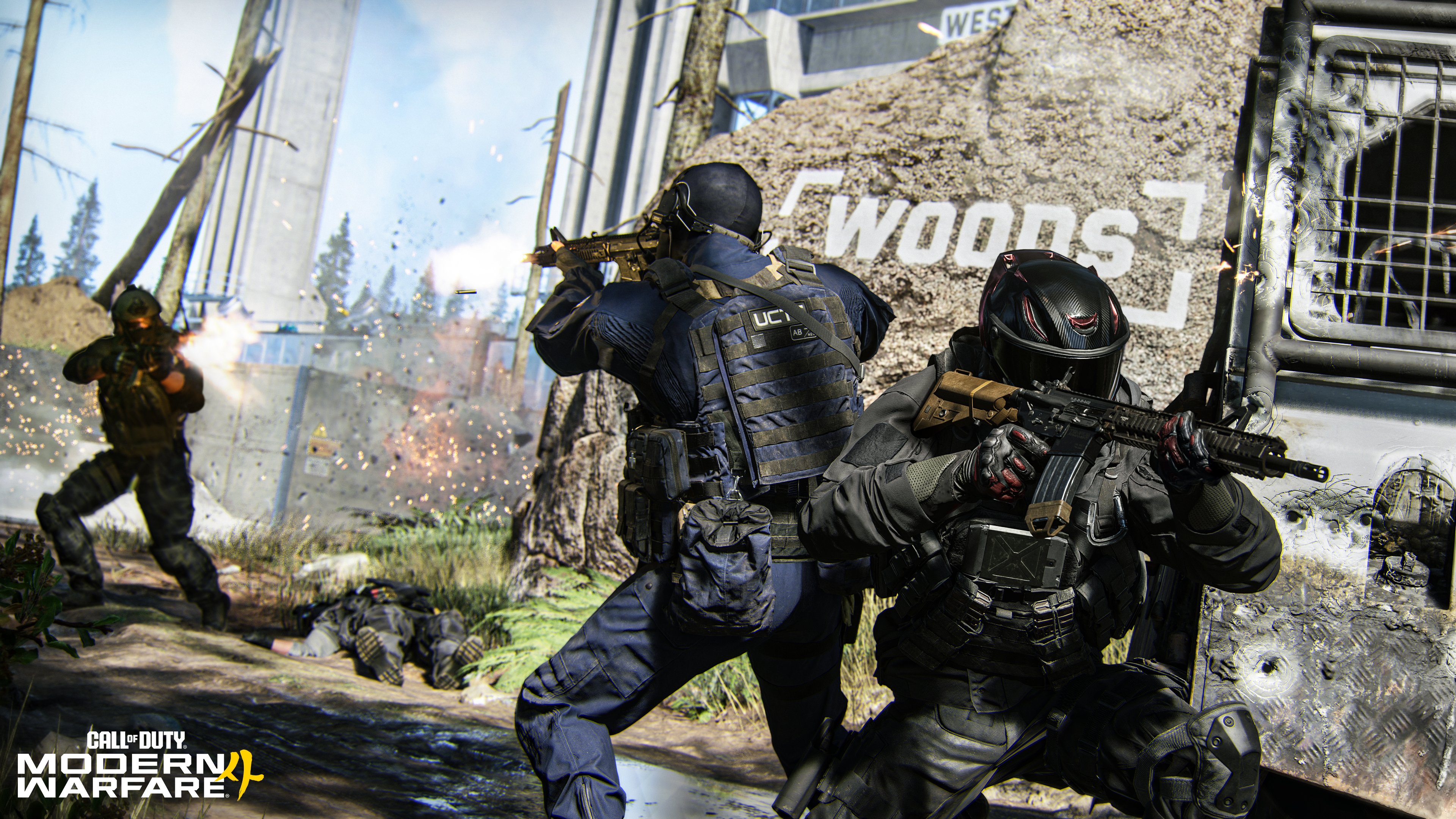 Screenshot from the video game Call of Duty: Modern Warfare II showing two masked, armed tactical operators taking cover beside a damaged armored vehicle marked "WOODS" during a firefight.