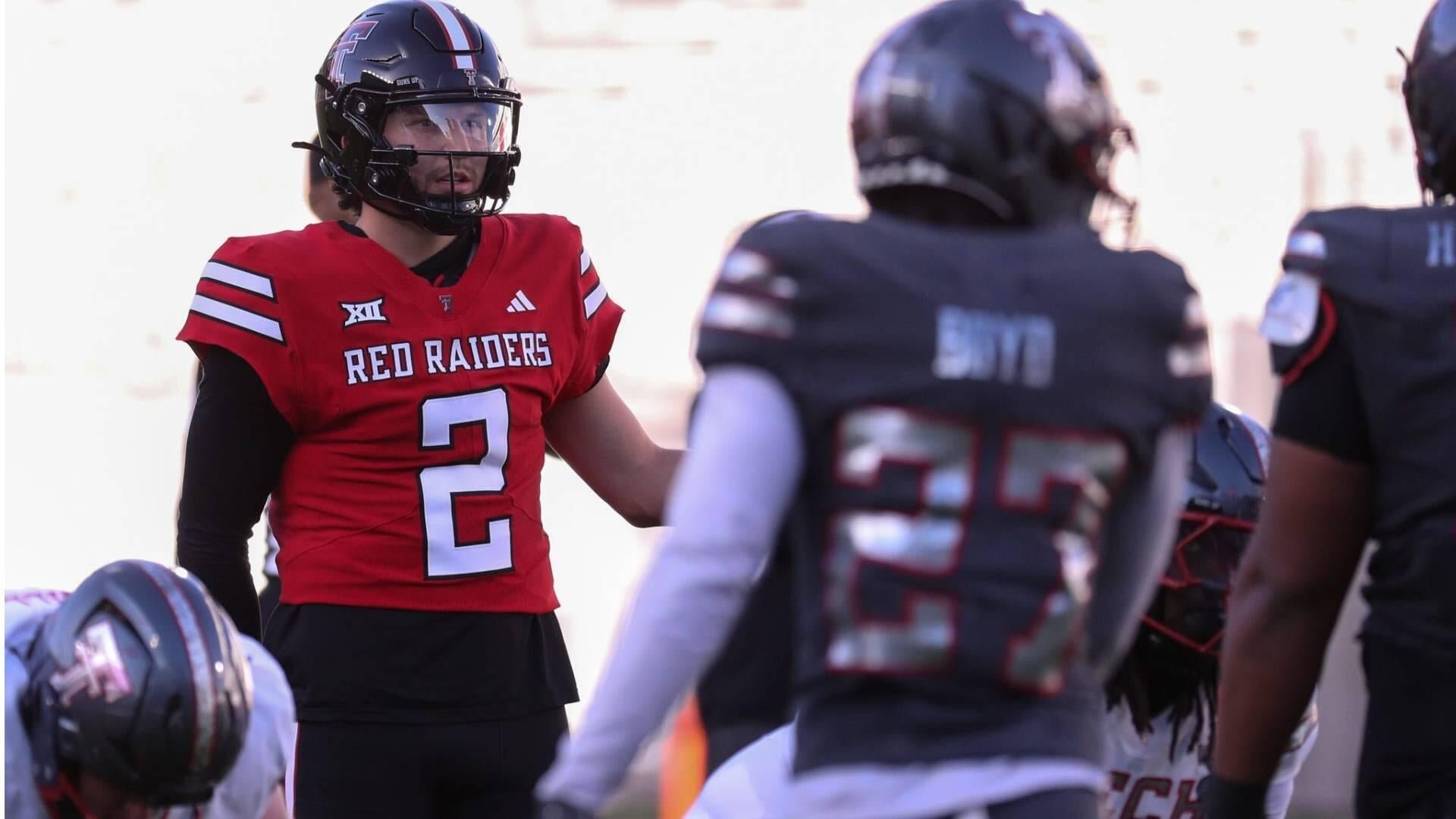 Texas Tech Red Raiders football player wearing jersey number 2 stands on the field facing opposing players in dark uniforms.
