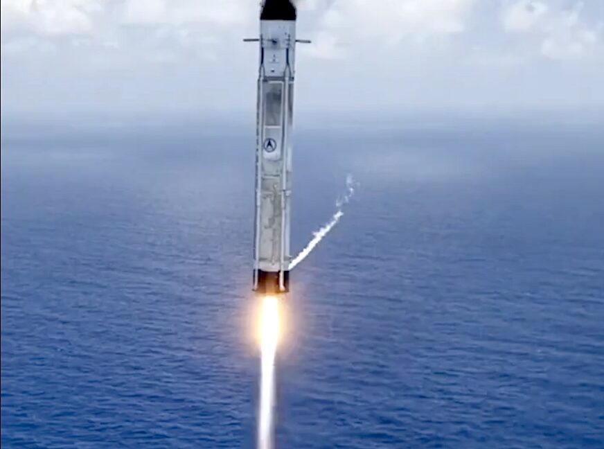 A rocket lifts off at night from a launch pad, its engine flame illuminating billowing smoke and surrounding ground equipment.