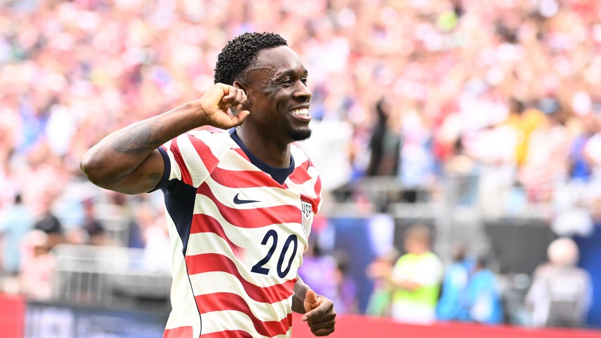 Two USA national team soccer players in red-and-white striped jerseys celebrate on the pitch, with a McDonald's advertising board and crowd visible behind them.