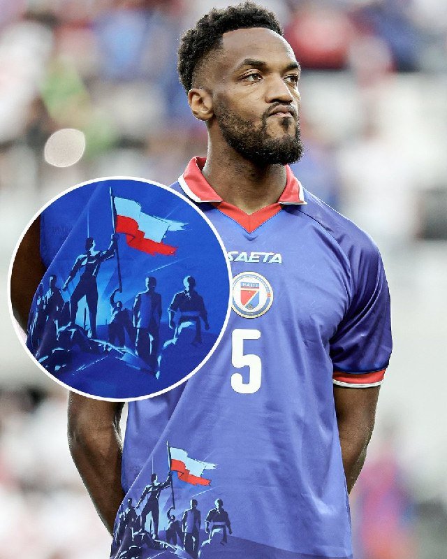 A bearded soccer player wearing a blue Haiti national team jersey with the number 5 stands in a stadium, with an inset graphic showing figures raising a Haitian flag.