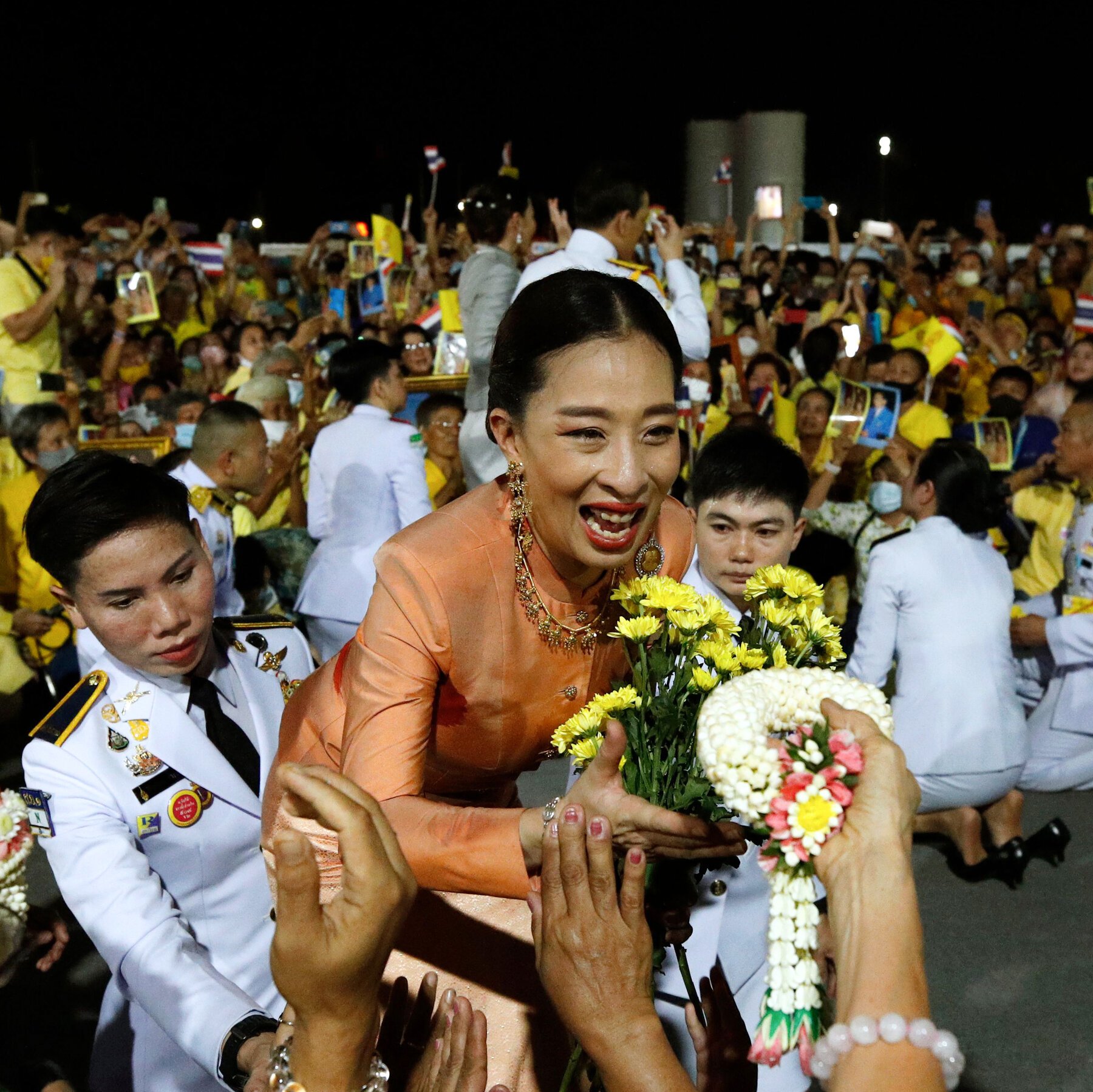 A woman in a purple formal outfit and sash smiles in a regal setting with floral arrangements, beneath a news headline identifying her as Princess Bajrakitiyabha of Thailand.