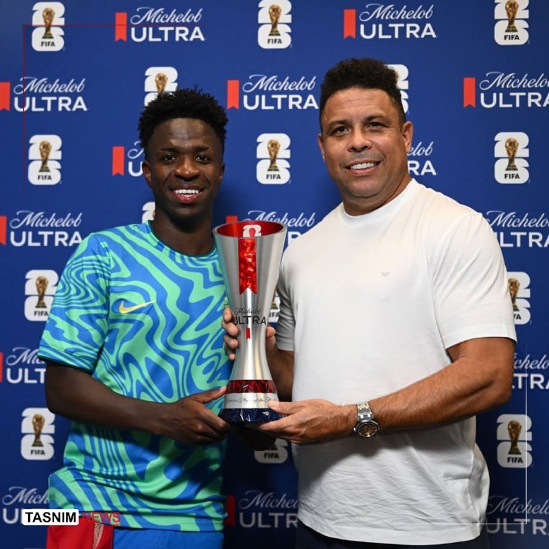 Two smiling men pose while holding a silver Michelob ULTRA FIFA trophy in front of a branded backdrop.