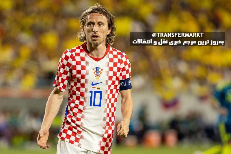 A long-haired soccer player wearing a red-and-white checkered jersey with the number 10 stands on a field before a blurred crowd, with a "@TRANSFERMARKT" watermark visible.