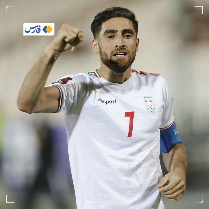 A bearded soccer player wearing a white jersey with the number 7 and a captain's armband raises a clenched fist in celebration during a match.