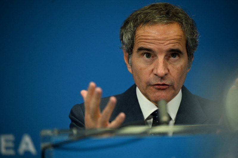 A gray-haired man in a dark suit gestures with his raised hand while speaking at a podium against a blue backdrop displaying partial "EA" lettering.