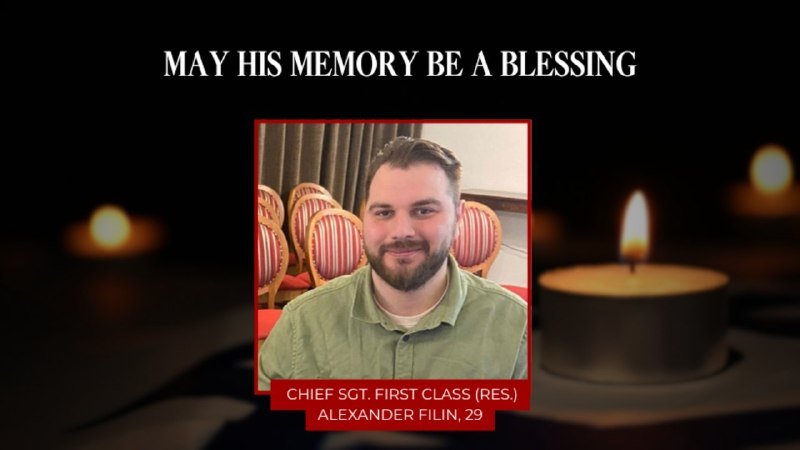 A memorial graphic displays the text "MAY HIS MEMORY BE A BLESSING" above a photo of a bearded man in a green shirt, identified as "CHIEF SGT. FIRST CLASS (RES.) ALEXANDER FILIN, 29," with lit candles in the background.