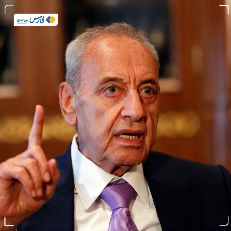 Two men in dark suits stand facing each other in profile before an Israeli flag, with one man extending his index finger toward the other.