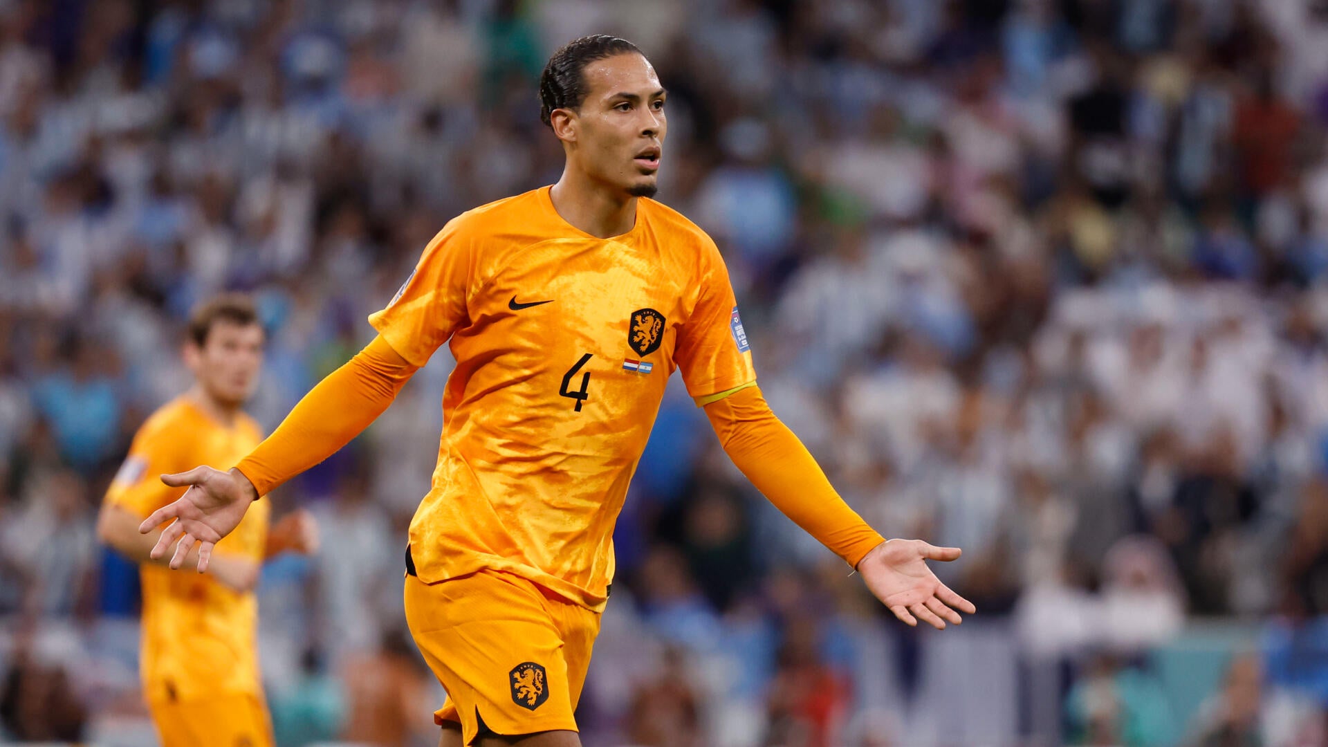 A player in a yellow jersey strikes the ball while a white-jerseyed opponent challenges him during a soccer match in a crowded stadium.