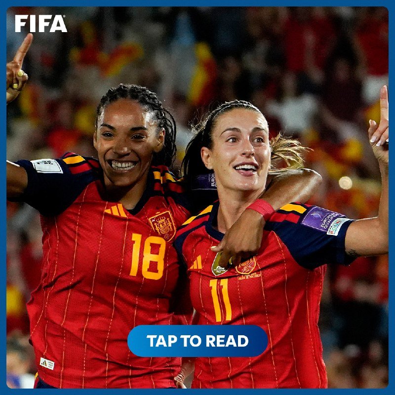 Two female soccer players in red Spain jerseys (numbers 18 and 11) celebrate with raised arms in front of a crowd, with a "FIFA" logo and "TAP TO READ" button visible.