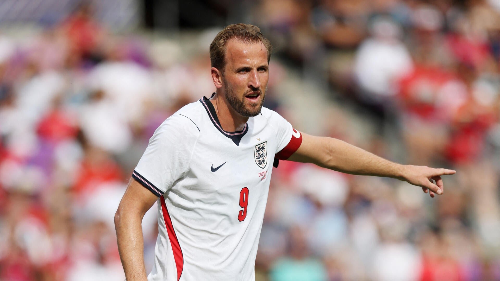 A bearded soccer player wearing a white England jersey with the number 9 points to the right during a match.