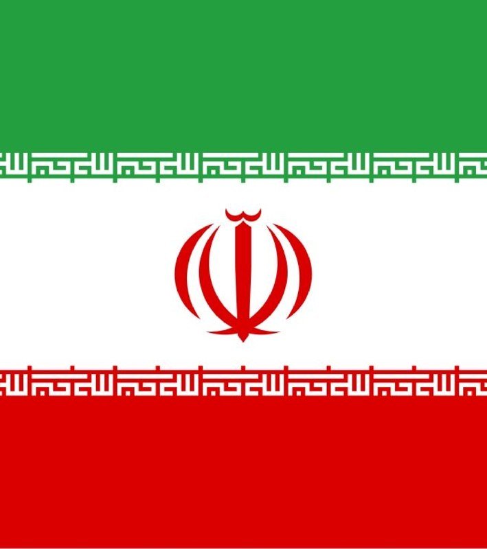 A man in a dark suit speaks at a podium bearing an emblem, flanked by two Iranian flags against a blue backdrop displaying a world map and "Ministry of Foreign Affairs."