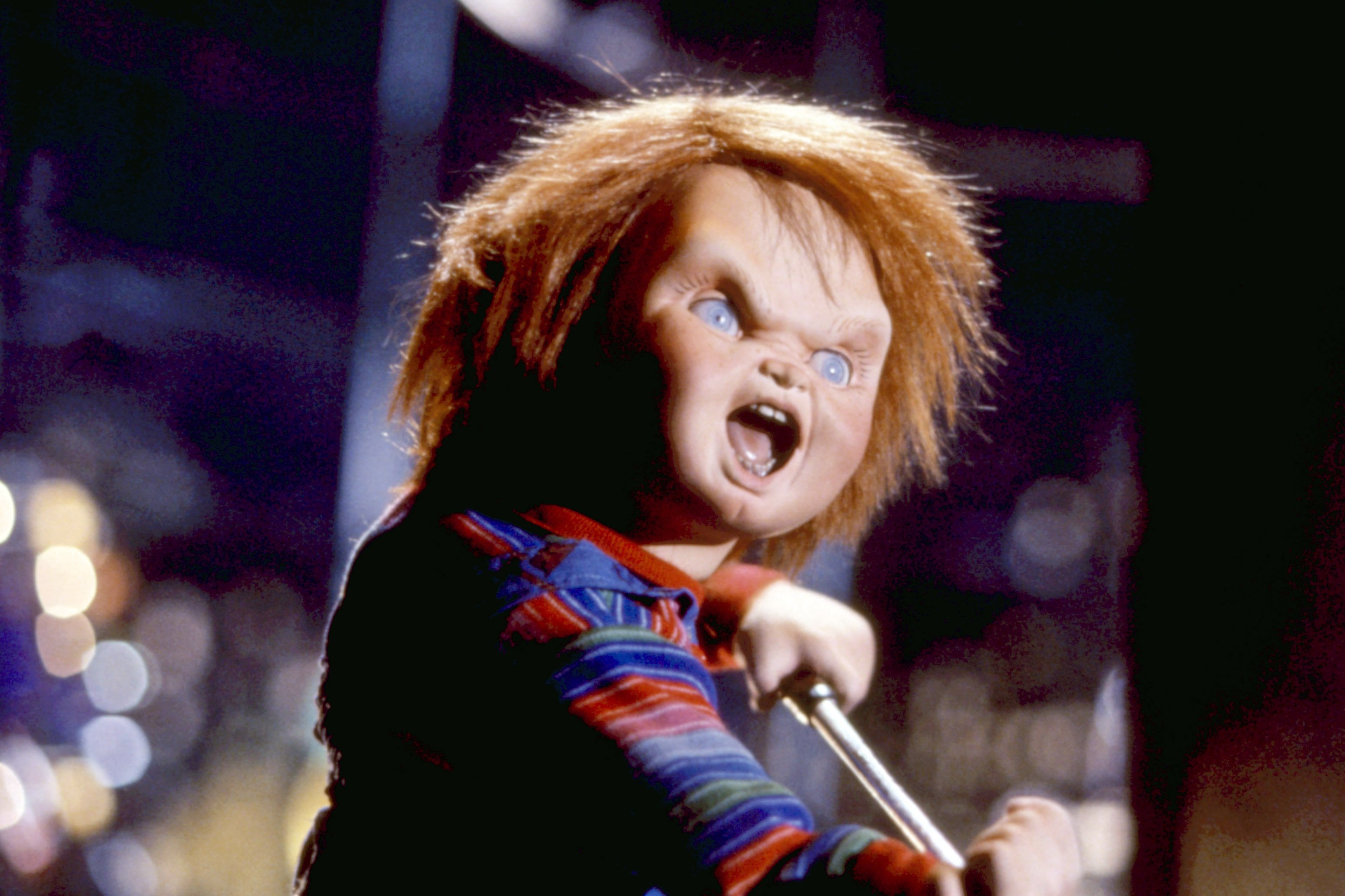 A doll with orange hair and a striped shirt holds a microphone and shouts with its mouth open.