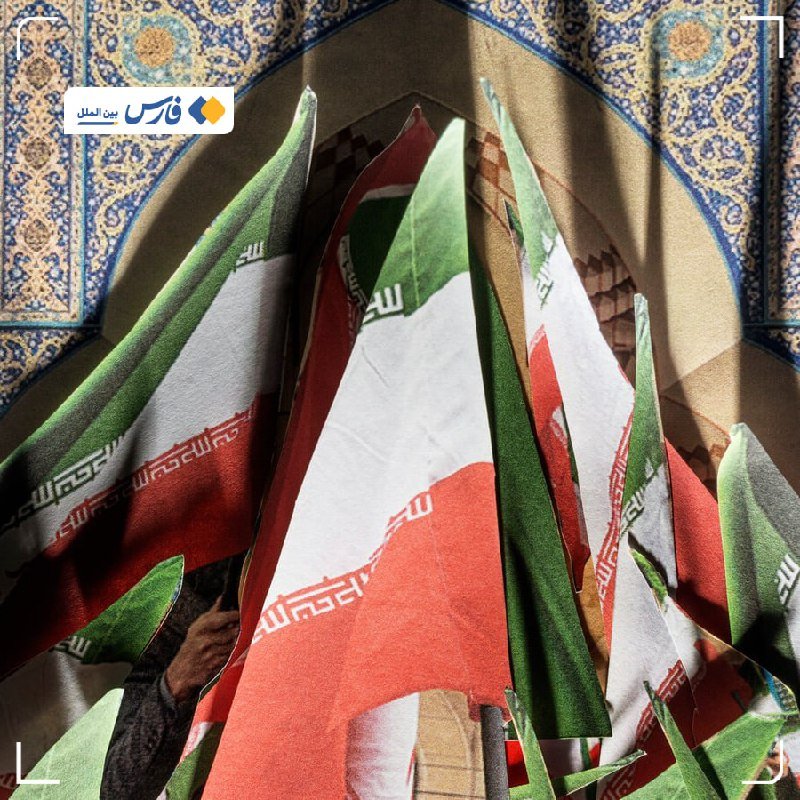 Multiple Iranian flags with green, white, and red stripes are displayed beneath an ornate blue-tiled archway.