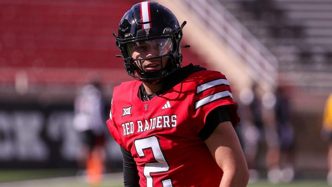A football player wearing a red "Red Raiders" jersey with the number 2 and a black helmet stands on the field, with stadium seating visible behind him.