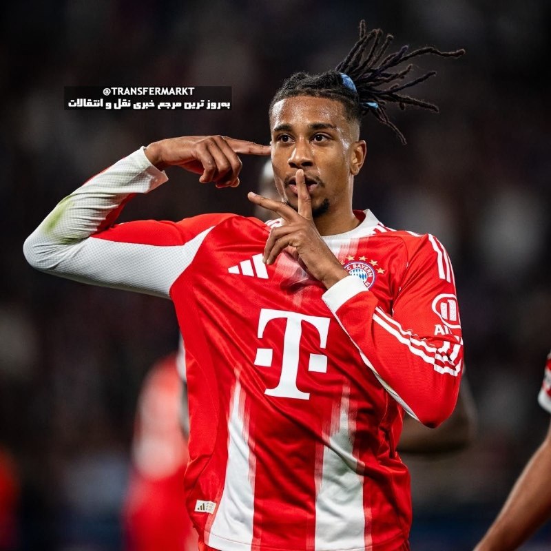 A smiling soccer player with braided hair, wearing a red Puma jersey, celebrates with outstretched arms in a packed stadium.